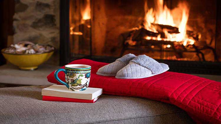 Books, hot beverage, red blanket and slippers in front of fireplace.