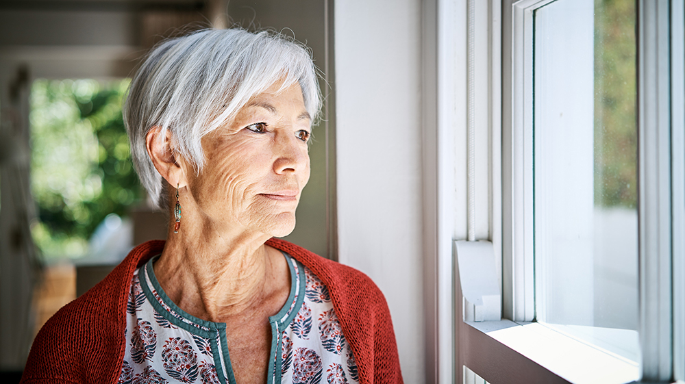 Older woman in a red cardigan gazing out a window.