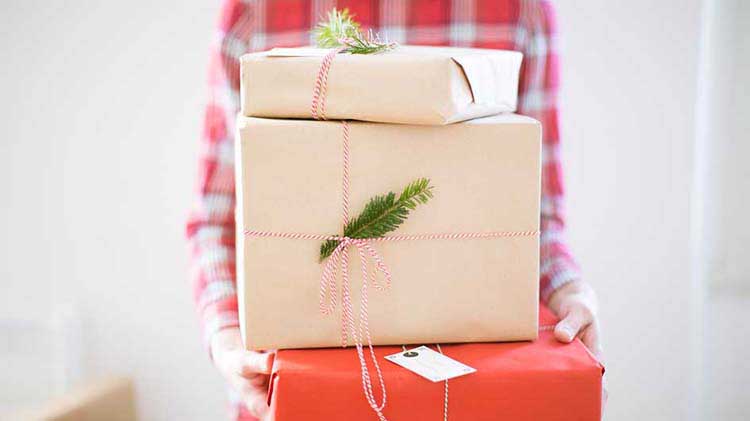A woman holds a stack of holiday gift packages wrapped in kraft paper.