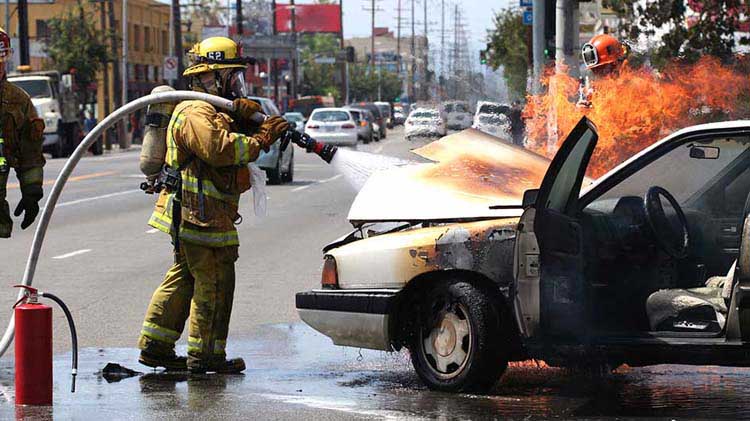 Fireman spraying water under the hood of a car on fire.