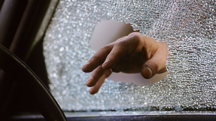 A hand reaches through a hole of a shattered side window.