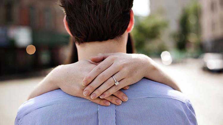 Hands with engagement ring embracing man.