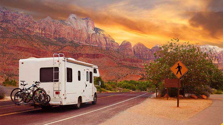 RV on the road with mountains and sunset.