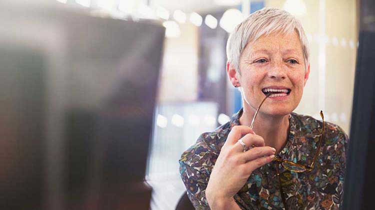 A mature woman holding eye glasses looking at her retirement investment portfolio on her laptop.