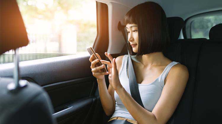 Image of a woman sitting in a car using a cell phone.