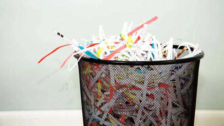 Black waste basket full of shredded paper.