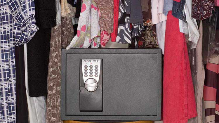 A safe that contains personal assets is sitting among hanging clothes in a closet