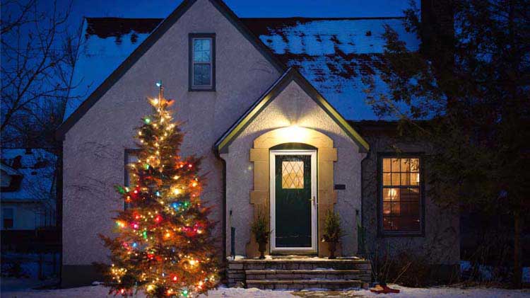 Cozy house in the evening with a lit up Christmas tree outside.