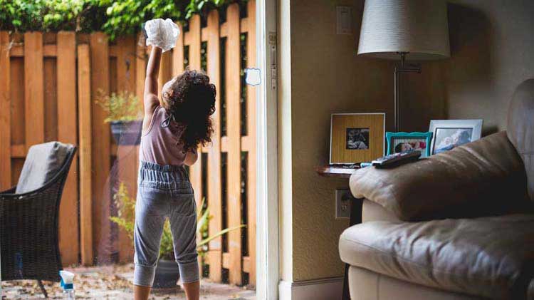 Little girl spring cleaning a glass sliding door.