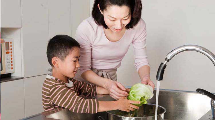 Mom with her son washing produce in the kitchen sink to remove pesticides.