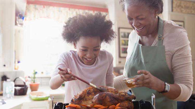 Grandmother and granddaughter cooking and basting a turkey in the kitchen.