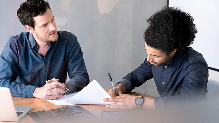 Two men sitting at a table and one of them is signing a car loan.