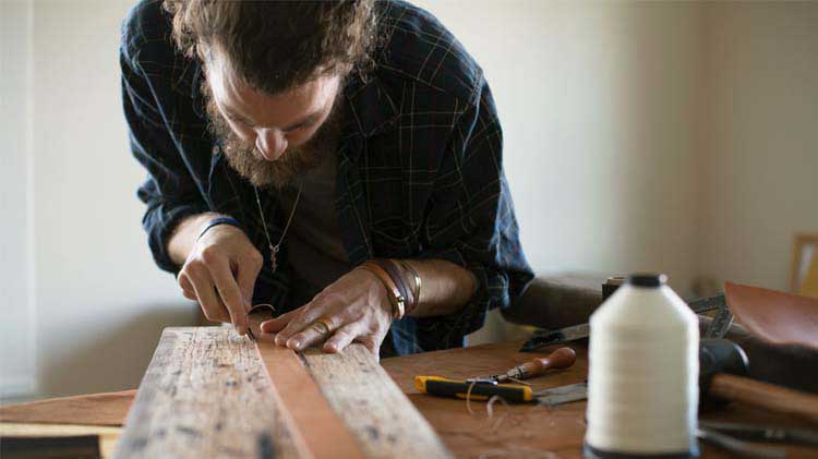Man crafting a belt on a table as a way to make money from home.