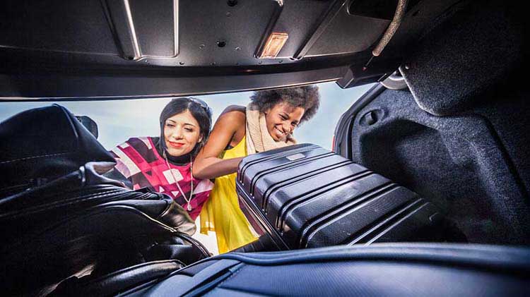 Women putting suitcases into car trunk
