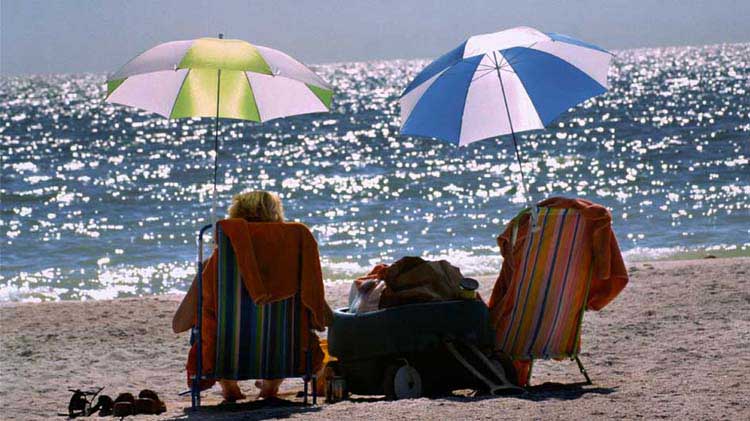 Older couple sitting on the beach under umbrellas