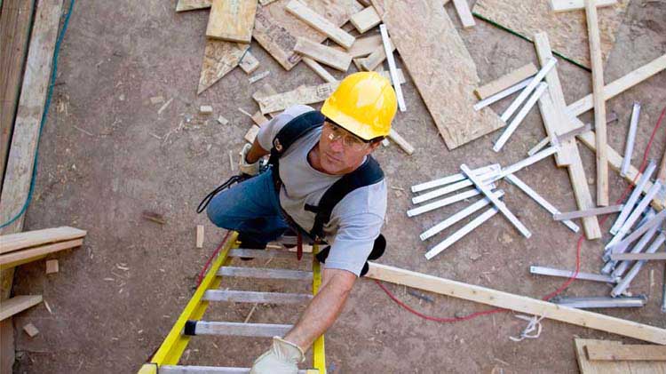 Man in hardhat looking upward as he begins safely climbing a ladder.