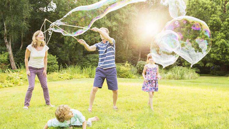 Family playing with giant soap bubbles in a yard.