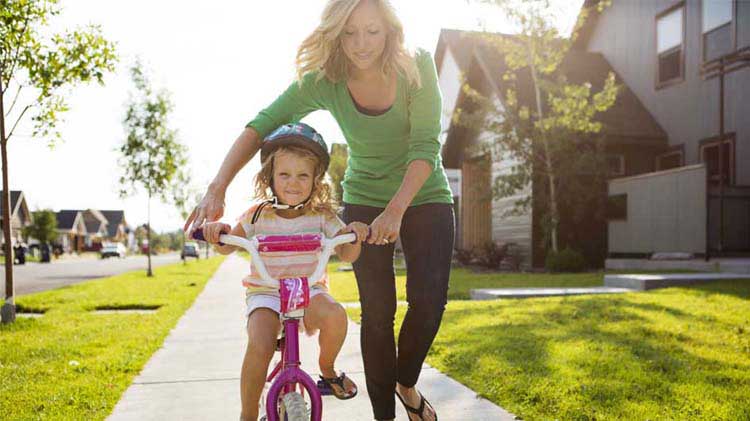 Mom helping young daughter learn to ride her bike.
