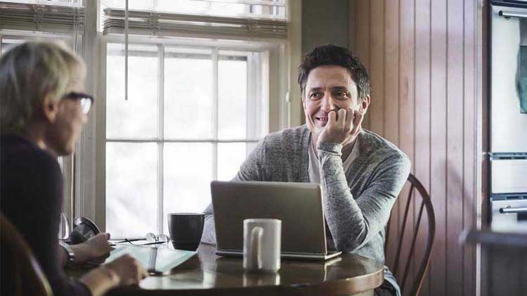 Men conversing in a coffee shop with a laptop.