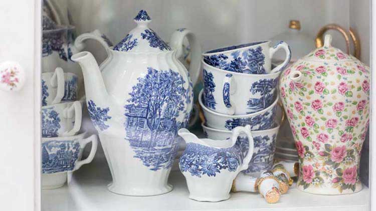 China tea pot, cream server, tea cups and other items on a shelf.