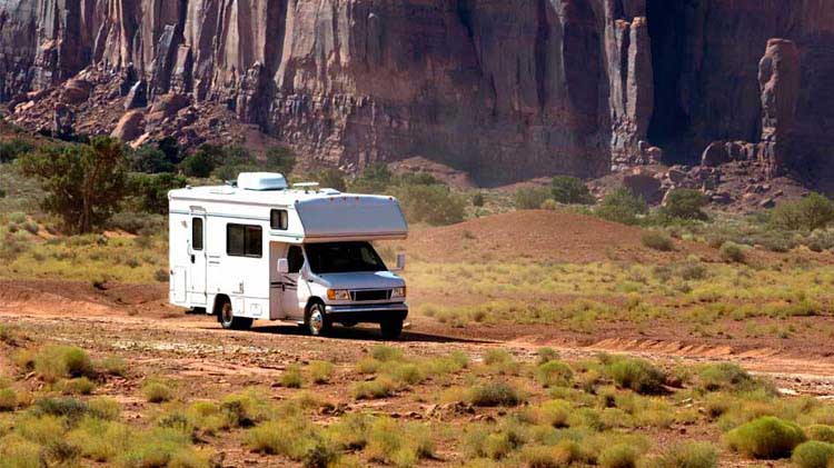 RV on a dirt road with mountains in the background.