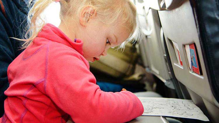 Toddler coloring a picture on a tray while safely traveling on an airplane.