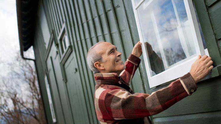 Un hombre le da mantenimiento a una vivienda histórica arreglando una ventana.