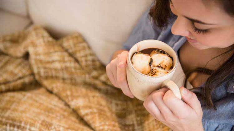 A woman enjoys her hot chocolate while covering up with an electric blanket.