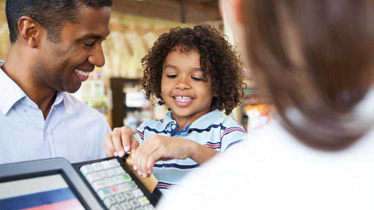A dad is letting his young son hold his credit card to swipe at a store cash register.