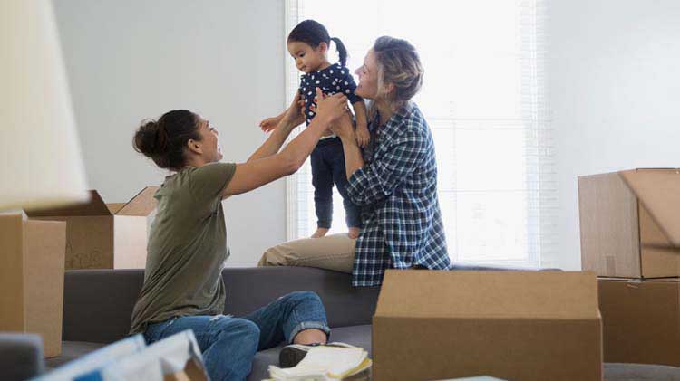 Two women and a little girl playing in a room full of moving boxes.