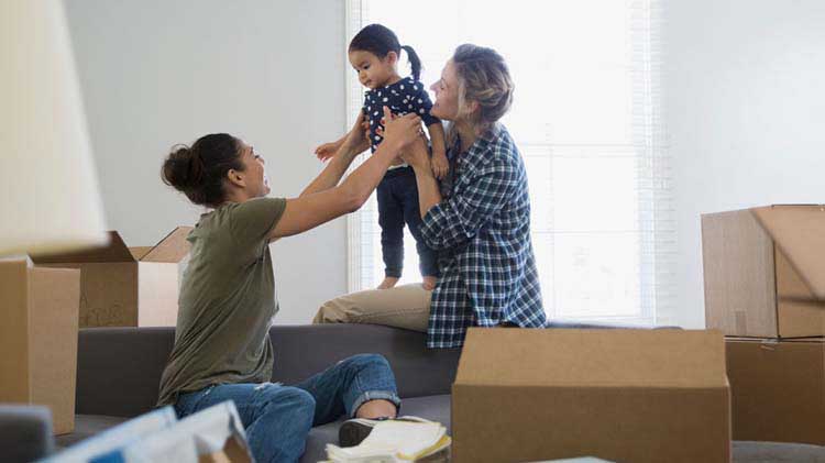 Dos mujeres juegan con una niña en una habitación llena de cajas de mudanza.