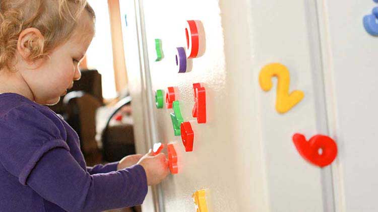 Toddler playing with refrigerator magnets that could cause a household hazard.