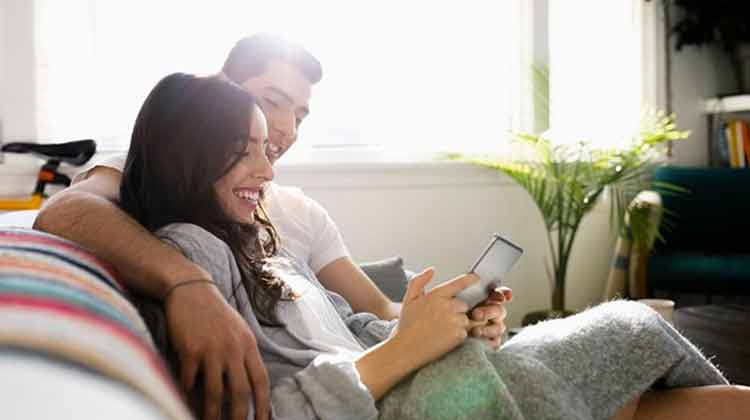Man and woman sitting on couch looking at tablet and discussing refinancing.