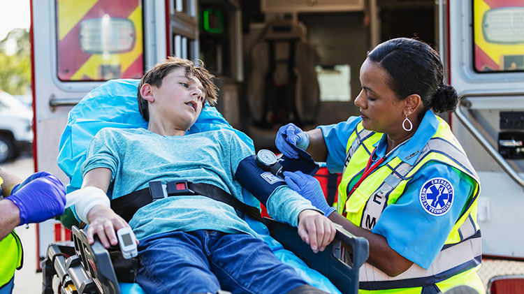 A young boy watches as an emergency responder checks his blood pressure while he’s strapped to a gurney.