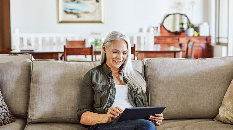 Older woman working on tablet computer on couch at home.