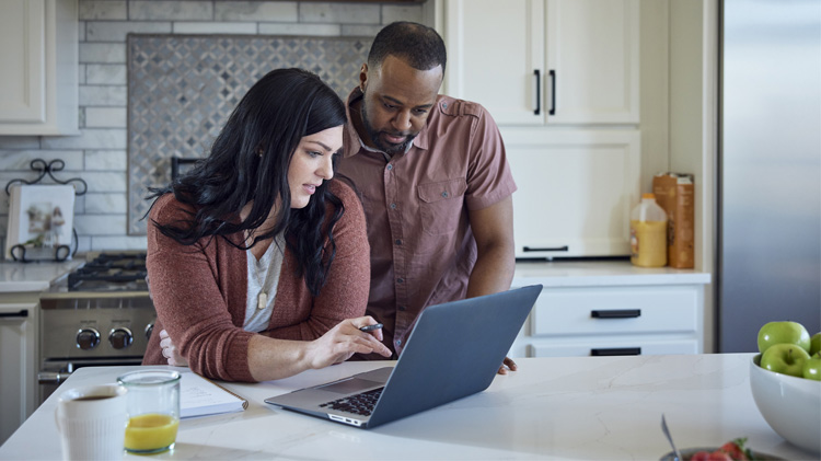 A couple in their kitchen applying for car insurance on their laptop.