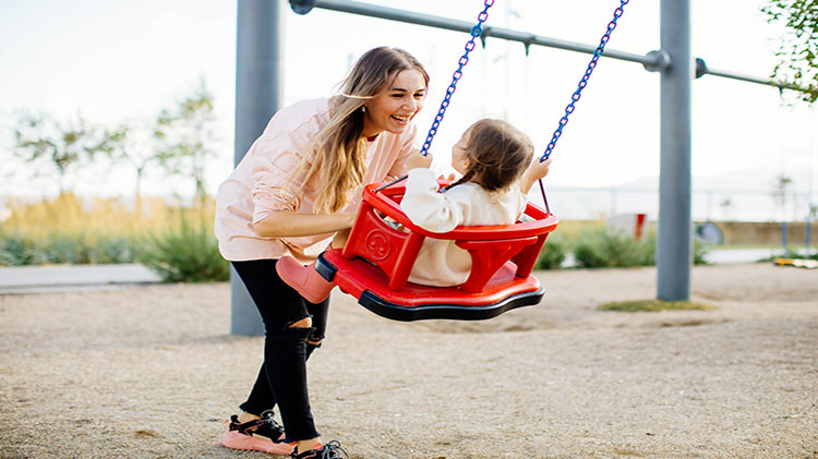 Mother pushing child on playground swing. 