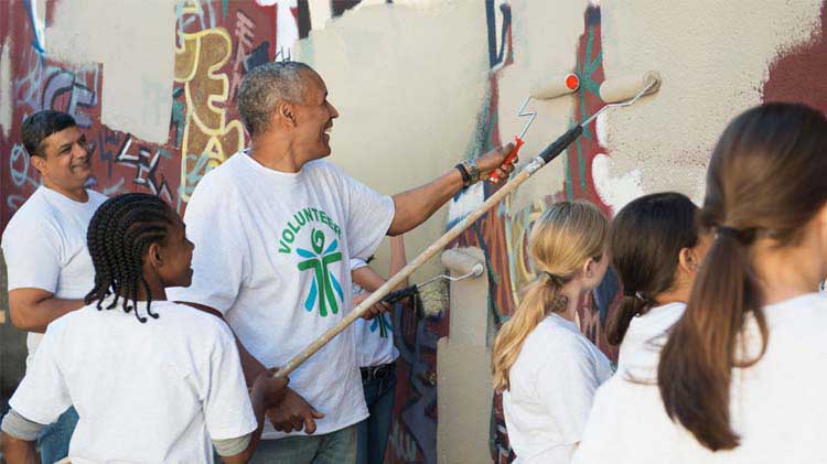 Group of people painting over graffiti on a wall.