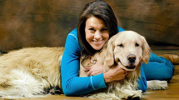 Woman lying on the floor hugging her golden retriever.