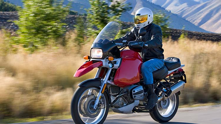 Man riding a red motorcycle with hills in the background.