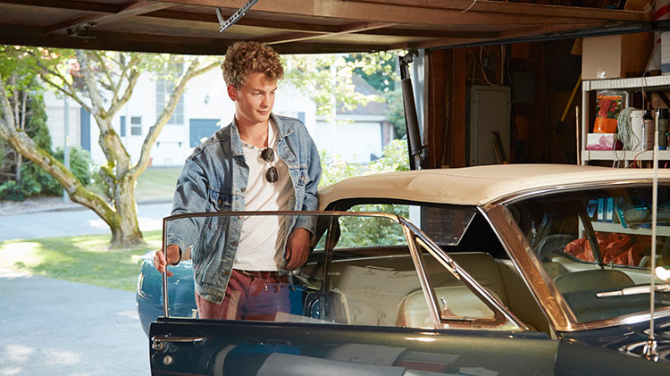 Young man in a garage opening door of vintage car.