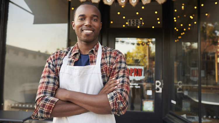 An African American man stands in front of his small business.