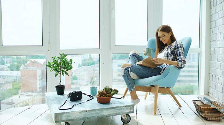 Mujer lee en una silla frente a la ventana, feliz de haber comprado un condo