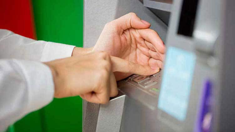 Person's hand entering a PIN number at an ATM machine.