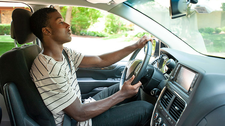 A young man is driving his car, wearing his seat belt and practicing defensive driving