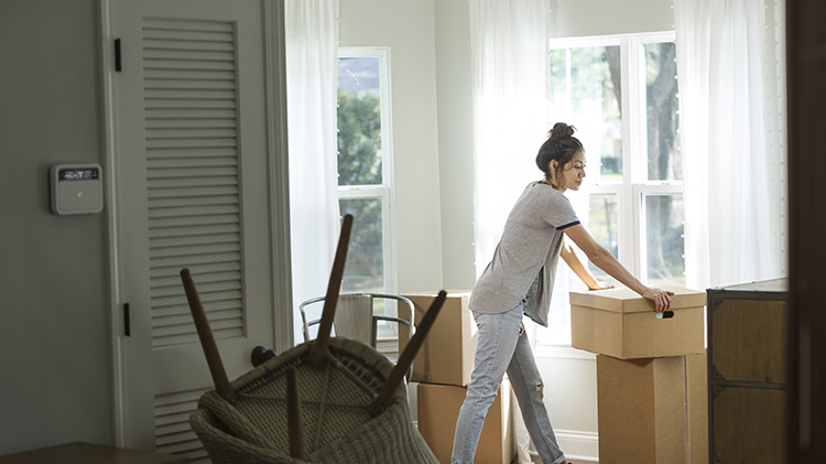 A woman leans against a packing box while packing to move after her divorce