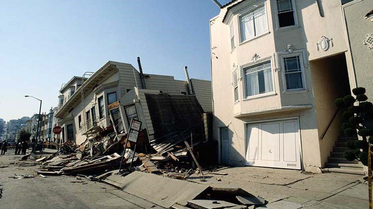 Houses with earthquake damage where one is leaning to the left and sunk in.