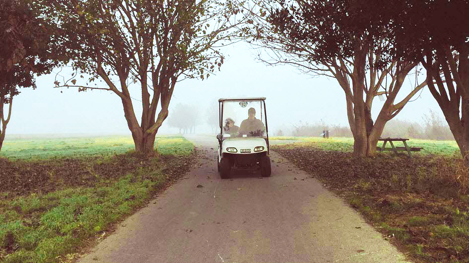 Man and child on a foggy golf course driving a golf cart
