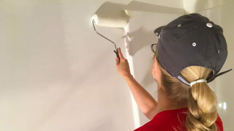 Woman in red shirt painting a wall during home maintenance.