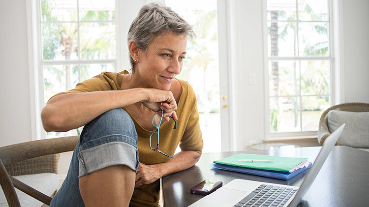 Woman looking at a laptop and thinking about a retirement plan.